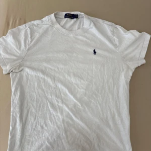 Vit t-shirt från Polo Ralph Lauren - Vit slim fit t-shirt från Polo Ralph Lauren med klassisk rund hals och korta ärmar.Den är storlek M men funkar även för S. På bröstet finns den ikoniska broderade polospelaren i marinblått. T-shirten är gjord i mjuk bomull och har en clean, stilren look som funkar till allt.