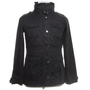  Peak Performance fieldjacket - Svart fieldjacket från Peak Performance med hög krage, flera fickor med knappar och dragkedja framtill. Jackan är i mycket bra skick. Perfekt för dig som vill ha en stilren och funktionell jacka.