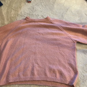 Ljusrosa stickad tröja från 157 - Mysig ljusrosa stickad tröja från 157 med rund halsringning och ribbade muddar. Perfekt för lager-på-lager och chill dagar. Enkel design som är lätt att matcha med jeans eller kjol.