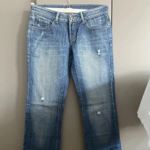Blå  jeans med slitningar 28/32 - Snygga blå jeans med slitna detaljer framtill. Klassisk femficksmodell med ljus tvätt och gul brodyr på bakfickorna. Jeansen har normal midja och är tillverkade i bomull för en skön känsla.