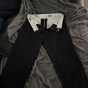 Svarta Dickies 874 byxor - Klassiska svarta Dickies 874 byxor med rak passform och stilren look. Byxorna har dragkedja och knapp framtill samt tydlig Dickies-märkning på insidan av linningen. Perfekta för dig som gillar streetwear och enkel stil.