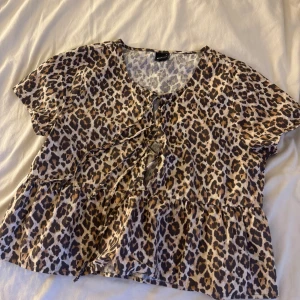 Leopardmönstrad blus från Gina Tricot - Säljer en snygg blus från Gina Tricot med leopardmönster i beige, brunt och svart. Blusen har korta ärmar, volang nedtill och snörning framtill.