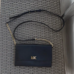 Svart Michael Kors väska - Superfin svart liten väska med gulddetaljer från Michael Kors. Jättefint skick, inga defekter! Justerbart axelband med kedja, väldigt många fack, varav ett med dragkedja. Öppnas/låses med genom att vrida på bokstaven (se bild 5). Mått: 21x13cm.  Nypris 2500kr.