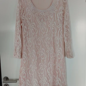 Ljusrosa spetsklänning från Cream - Superfin ljusrosa kortklänning från Cream med vackert blommigt spetsmönster och detaljerad broderad urringning. Klänningen har trekvartsärm och är fodrad undertill för en bekväm känsla. Perfekt för dig som gillar romantisk och feminin stil.
