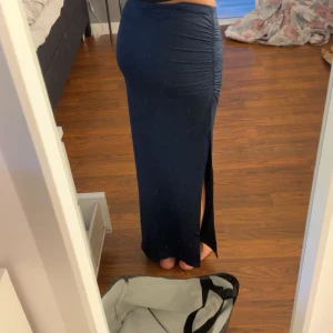 Mörkblå långkjol med slits - Snygg mörkblå långkjol med hög midja och tight passform. Kjolen har en cool slits på sidan och rynkade detaljer längs höften som ger en extra touch. Perfekt för dig som gillar stilrena och trendiga plagg. Storleken är Xs petite, så liten i storlek!