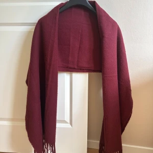 Vinröd halsduk med fransar - Mysig vinröd halsduk med fransar i ändarna. Tjockt och mjukt material som håller dig varm under kyliga dagar. Har blivit nopprig, men det kan man åtgärda med noppermaskin!