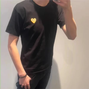 Svart Comme des Garçons Play t-shirt - Svart t-shirt från Comme des Garçons Play med det ikoniska gula hjärtat med ögon broderat på bröstet. Klassisk passform, rund hals och korta ärmar. Tillverkad i mjuk bomull, perfekt för en clean och stilren look.