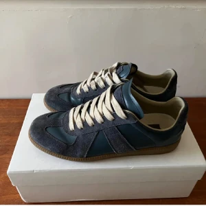 Maison margiela skor - Säljer ett par stilrena blå sneakers från Maison Margiela i storlek 43. Skorna har vita snören och är tillverkade i en mix av marinblå mocka och skinn. Skorna är endast testade och tveka inte att fråga om ni undrar något!