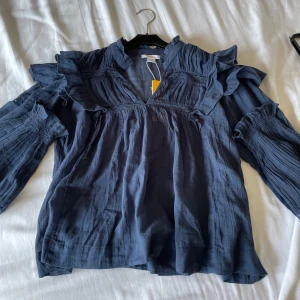 Mörk Blå blus med volanger  - Säljer en trendig mörk blå blus med volanger, vid axlarna. Tröjan är i linne material och perfekt nu till sommaren! Aldrig använd, lapp kvar. Passa på!!!😍🔥