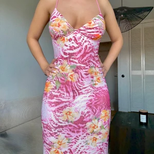 Rosa långklänning med blommor & öppen rygg - Långklänning i rosa och vitt med blommigt och zebramönster, tunna axelband och öppen rygg med snygga band och broderad fjäril. Figurnära passform och v-ringad framtill. Perfekt för sommarens varma dagar.