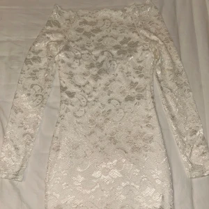 Vit/crèmefärgad spetsklänning från Model Behaviour - Supersnygg vit/crèmefärgad kortklänning från Model Behaviour i storlek XS. Klänningen har långärmade ärmar och är täckt av ett blommigt spetsmönster. Den är figurnära och har en offshoulder-design samt en vit tubklänning under med silikonband för att hålla klänningen på plats. 