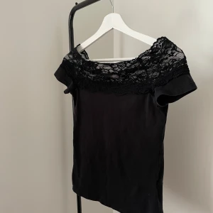 Svart offshoulder topp med spets - Snygg svart topp med offshoulder-modell och bred spets upptill. Fint skick. 