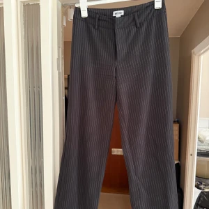 Svarta randiga kostymbyxor Madlady - Snygga svarta kostymbyxor från Madlady med tunna vita ränder. Byxorna har raka ben, medelhög midja och dubbla hällor med en knapp. Materialet är tunt och skönt trots att det ej är mycket stretch i de. Passar perfekt till en stilren look. Det finns inga fel alls på byxorna trots att jag använt de flitigt. 