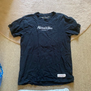 Svart t-shirt - Svart t-shirt från Mitchell & Ness med broderad logga på bröstet och patch nertill. Klassisk passform och rund hals. Tillverkad i mjuk bomull, perfekt för en chill och sportig look!🙌🏻