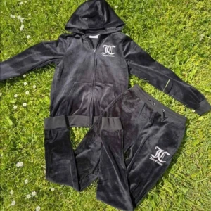 Juicy Couture svart velourset strl M till S - Juicy Couture mjukisset i svart velour med hoodie och byxa. Setet har dragkedja på tröjan, fickor och tydliga loggor fram och bak i vitt. Byxan har resår och snörning i midjan. Perfekt för en chill och trendig look.