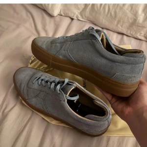 Blå mockasneakers från Axel Arigato - Snygga sneakers i ljusblå mocka från Axel Arigato med bruna gummisulor. Skorna har klassisk rund tå, platt sula och snörning framtill. Perfekta för dig som gillar stilrena och minimalistiska sneakers med premiumkänsla. Har lådan och allt og