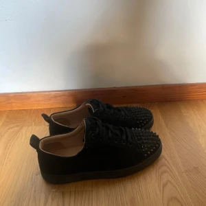 Svarta sneakers med nitar - Säljer ett par svarta Christian Louboutins med coola nitar på tån. storlek 39 fits 40/40,5 De har en klassisk snörning och en röd sula som ger en snygg kontrast. Perfekta för att ge din outfit en edgy touch! endast skor tillkommer använda i bra skick i 4/5 månader 