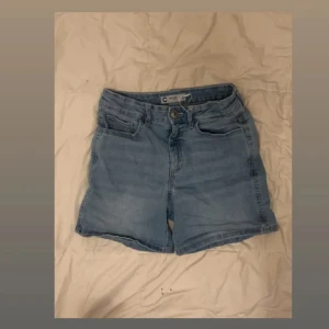 Ljusblå jeansshorts från Cubus - Snygga ljusblå jeansshorts från Cubus med klassisk femficksdesign och knappgylf. Perfekta för varma dagar och enkla att matcha med allt. Shortsen har en normal passform och är tillverkade i mjukt jeanstyg för extra komfort.