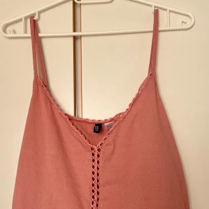 Rosa linnetopp med spets från H&M - Supersöt rosa linnetopp från H&M med tunna axelband och dekorativ spetskant längs ringningen och framtill. Toppen har en lätt A-linjeform och är tillverkad i ett mjukt bomullstyg. Perfekt för varma dagar och enkel att styla med jeans eller kjol.