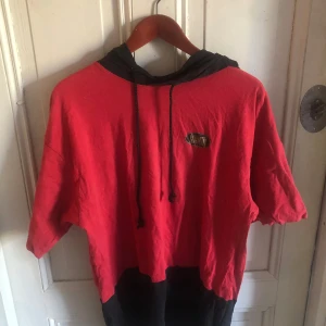 Röd och svart hoodie från Everlast - Cool hoodie från Everlast i rött och svart med stor logga både fram och bak. Tröjan har korta ärmar, svart huva med snörning och är gjord i mjuk bomull. Perfekt för en sportig och avslappnad stil.