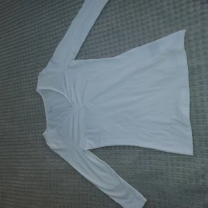 Vit långärmad topp från Å - Säljer en vit långärmad topp från Å med snygg rynkdetalj vid bysten. Tröjan har tre kvarts ärm. Modellen har en lätt v-ringad hals och är gjord i mjuk bomull, perfekt för dig som gillar en clean och enkel stil. Passar dig som vill ha en basic men ändå trendig topp.❤️