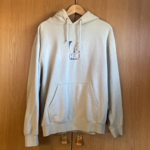 Beige hoodie från HUF med tryck - Snygg beige hoodie från HUF med färgglatt tryck på bröstet. Klassisk känguruficka, snöre i huvan och mjukt material. Nån fläck men i övrigt toppskick. Priset är inte hugget i sten. 