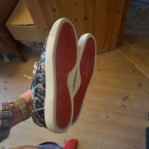Christian Louboutin sneakers - Snygga sneakers från Christian Louboutin med svartvitt grafiskt mönster och klassisk röd sula. Säljer skorna då de är aningen små på mig. Mycket fint skick, men tecken på användning på vissa platser som knappt syns. Skorna är perfekta  för dig som vill sticka ut med exklusiva detaljer. Egna och otroligt snygga. Passar 42-43. Orginallåda och äkthetsbevis tillkommer givetvis.