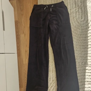 Svarta mjukisbyxor Juicy Couture - Mysiga svarta mjukisbyxor från Juicy Couture med breda ben, stora fickor fram och bak samt snörning i midjan. Byxorna är i mjuk velour och har snygga Juicy Couture-detaljer på knapparna. Perfekta för chill dagar eller när du vill vara extra comfy💖