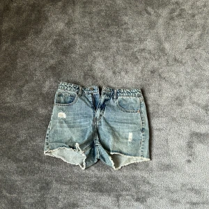 Blå jeansshorts från LAB Industries - Snygga blå jeansshorts från LAB Industries med hög midja och råa, fransiga kanter. Shortsen har slitna detaljer framtill och klassiska fem fickor. Perfekta för sommaren och ger en cool, avslappnad vibe.