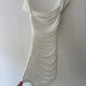 Vit draperad kortklänning - Supersnygg vit kortklänning med draperad effekt och offshoulder-design. Klänningen har en markerad dragkedja bak och är figurnära med snygga rynkade detaljer. Tog på mig den till min student. 