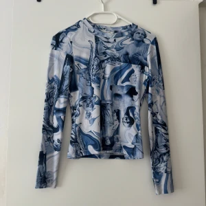 Blåvit långärmad topp från Monki XS - Säljer en långärmad topp från Monki i storlek XS (satt bra på mig som har storlek S) med unikt blåvitt mönster av statyer och konstnärliga motiv. Tight passform och tillverkad i stretchigt syntetmaterial. 