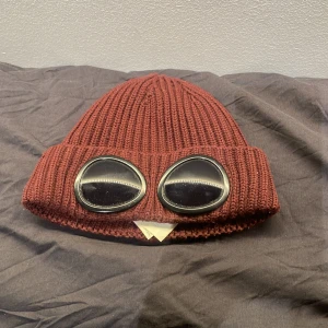 Vinröd stickad mössa från CP Company  - Snygg vinröd mössa från CP Company. Mössan är äkta och andvänd en del, men fortfarande i bra skick! Har ni frågor angående pris eller annat är det bara att skriva:)