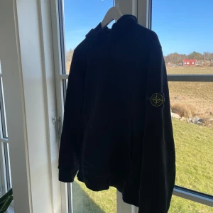 Svart hoodie från Stone Island - Säljer en svart hoodie från Stone Island med deras ikoniska märke på ärmen. Inköpt på nk 2024 så kvitto samt tags finns kvar, storlek M så passar S/M. Fint cond tvättad en gång endast