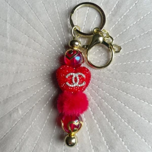 Nyckelring med rött hjärta och pärlor - Snygg nyckelring med ett glittrigt rött hjärta och pärlor. Den har en guldfärgad ring och klämma för enkel fastsättning. Perfekt accessoar för att ge din väska eller nycklar en personlig touch.