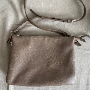 Brun axelväska  - Säljer en stilren brun axelväska med justerbar rem och praktisk dragkedja. Väskan har flera fack inuti. Föremommer defekter.