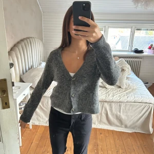 Grå kofta från Ganni - Säljer en stilren grå kofta från Ganni. Koftan har långa ärmar och knappar framtill, perfekt för kyligare dagar. Den är mjuk och bekväm, vilket gör den till ett utmärkt tillskott i garderoben. Passar bra till både jeans och kjol. Material alpacka och ull!