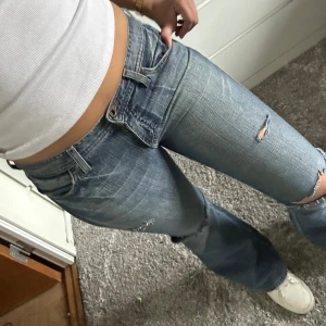 Blå bootcut jeans med slitningar - Snygga blå bootcut jeans med slitningar på knäna och låren. De har en klassisk femficksdesign och är lågmidjade för en avslappnad look. Perfekta för en trendig stil. Midjemått 41 cm  innerbenlängd 80cm