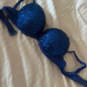 Blå paljettprydd bh från Gina Tricot - Säljer en blå bh från Gina Tricot med glittrande paljetter på kuporna. Den har justerbara axelband och en klassisk knäppning i ryggen. Perfekt för att lägga till lite extra bling i garderoben! Storlek 75A. Lite pusch up 
