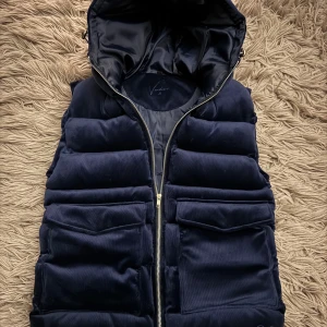 Vendera väst - Snygg mörkblå väst från Vendera med dragkedja och huva. Tillverkad i 100% polyester, perfekt för kyligare dagar. Västen har praktiska fickor framtill och en stilren design. De är nästintill nytt skit, använd ett fåtal gånger. Bara att skriva vid minsta fundering!💙🩶