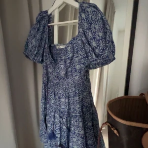 Blå blommig klänning från Zara - Charmig blå klänning från Zara med ett vackert blommönster. Klänningen har puffiga kortärmar och en v-ringad design. Perfekt för en somrig look! Säljer då jag inte använder den men tycker den är så fin och därav synd att bara ha den hängandes i garderoben🤗🩷 priset går att diskutera 