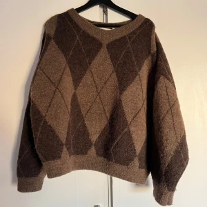 Brun mönstrad tröja från Carin Wester - Säljer en snygg brun tröja från Carin Wester med ett klassiskt rutmönster i olika nyanser av brunt. Tröjan har en rund halsringning och långa ärmar. 🧡