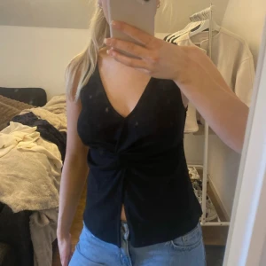 Svart söt topp - Snygg svart ärmlös topp med v-ringning och knytdetalj framtill. Perfekt för en stilren look. Tillverkad i ett mjukt och bekvämt material.