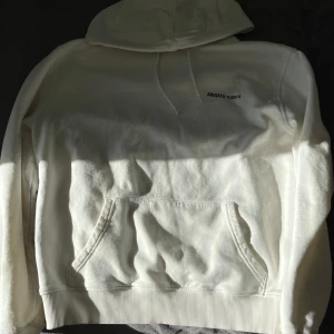 Vit hoodie från Axel Arigato - Säljer en stilren vit hoodie från Axel Arigato med tryck på bröstet och ryggen. Hoodien har en klassisk känguruficka och ribbade muddar vid ärmslut och nederkant. Perfekt för en avslappnad look.