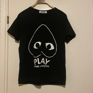 Svart t-shirt från Comme des Garçons - Snygg svart t-shirt från Comme des Garçons med det ikoniska hjärtmotivet och texten 'PLAY' på framsidan. Perfekt för en stilren och modern look. Skick 10/10 i princip oanvänd, bara testad.