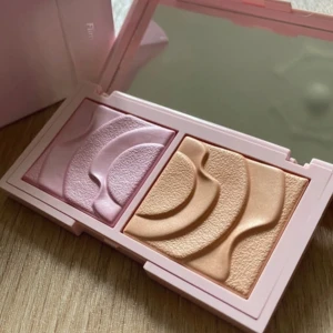 Highlighter och rouge från CAIA - Snygg duo med highlighter och rouge från CAIA i nyansen 'Flirty'. Kompakt förpackning i ljusrosa med spegel. Perfekt för att ge ansiktet en fräsch och strålande look. Helt ny, aldrig använd