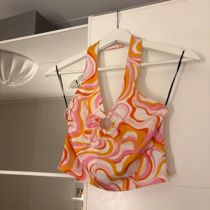 Färgglad halterneck topp med  mönster - Säljer en färgglad halterneck topp med ett mönster i rosa, orange och vitt. Hör av er vid funderingar eller om ni vill ha bilder med hur plagget sitter på mig. Titta gärna in mina andra plagg!