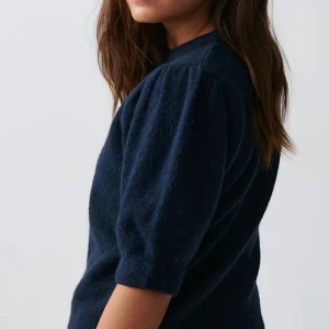 Mörkblå stickad tröja - Säljer en stilren mörkblå stickad tröja med puffiga trekvartsärmar. Perfekt för en avslappnad men chic look. Tröjan har en rund halsringning och ribbade kanter.