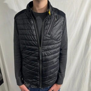 Parajumper väst - Stilig väst från Parajumpers i färgen svart, storleken är Y-L som motsvarar S i herrstorlek. Västen har ganska smal passform. Det är en lite tunnare dunväst som passar perfekt till våren.         Skick 9/10