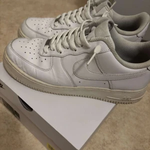 Nikr Airforce 1 - Säljer ett par klassiska vita Nike Air Force sneakers. Skorna har en stilren design med perforerade detaljer på tån och snörning framtill. De är tillverkade i skinn och har en bekväm passform. De finns bara ett litet svart märke där bakom på en sko som man lätt kan måla bort osv men annars helt nya och inga hål
