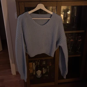 Ljusblå stickad tröja - Säljer en mysig ljusblå stickad tröja med v-ringning. Tröjan har långa ärmar och en croppad passform, perfekt för kyliga dagar. Den ribbade strukturen ger en stilren look. Passar bra till både jeans och kjol.